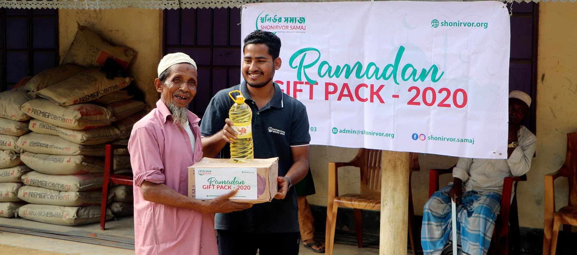 A Shonirvor Samaj volunteer handing a Ramadan gift pack to an elderly man