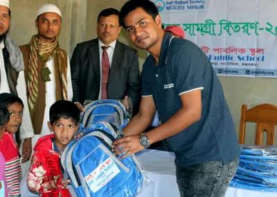A volunteer handing a blue school bag to a young boy