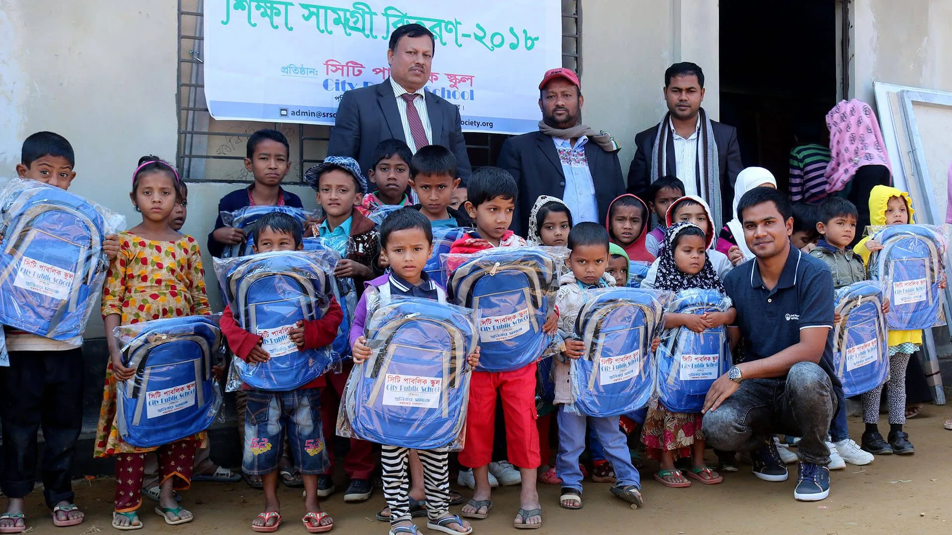 Children holding new school bags at a school materials distribution