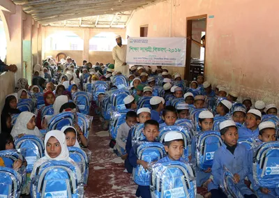 Rows of seated children holding new blue school bags inside a hall