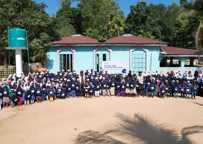Pupils with new school bags gathered outside a blue school building at the 2022 school bag distribution