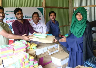Volunteers handing exercise books and stationery to a girl in a green headscarf