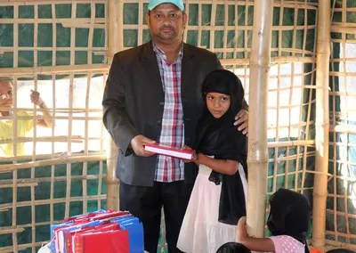 A man presenting a girl with school supplies inside a bamboo classroom