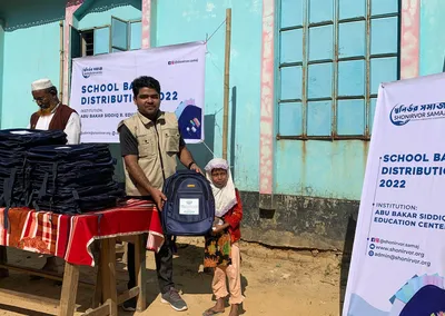 A volunteer handing a school bag to a girl at Abu Bakar Siddiq R. Education Center, 2022