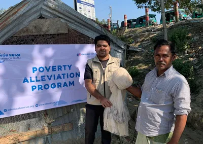 A volunteer handing a fishing net to a man in front of a Poverty Alleviation Program banner