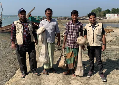 Volunteers with two fishermen holding new fishing nets on a riverbank