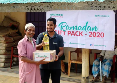 A volunteer handing a Ramadan gift pack and cooking oil to an elderly man