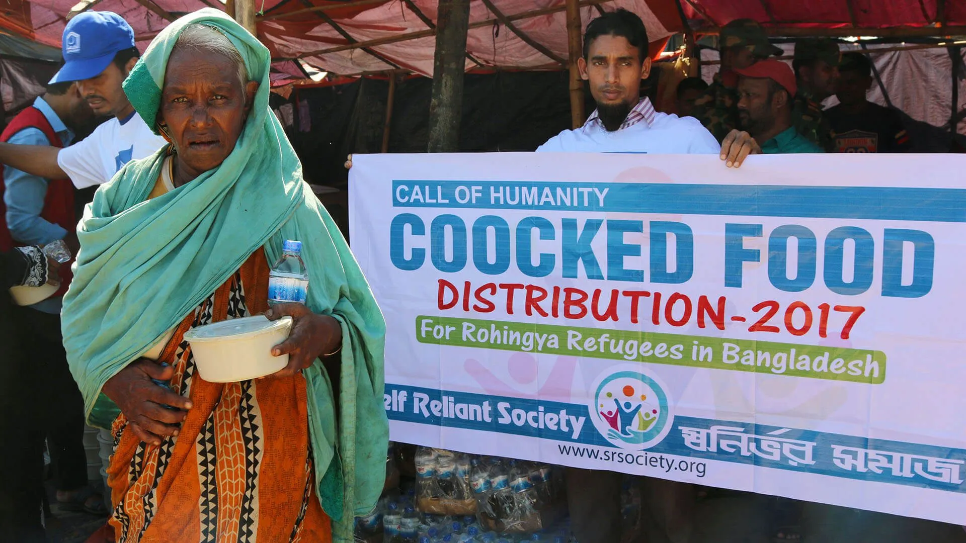 An elderly woman holding a meal at a cooked food distribution for Rohingya refugees