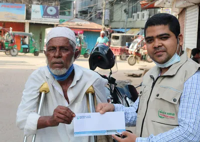 A volunteer handing an envelope to an elderly man on crutches