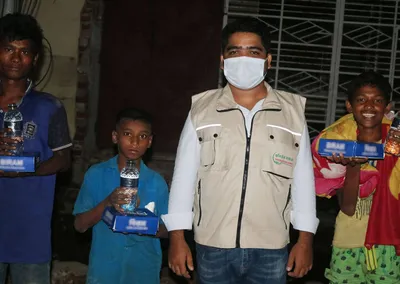 A volunteer with boys holding food packs and bottles of water
