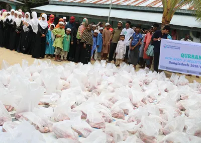 Bags of Qurban meat laid out in front of a long line of waiting families