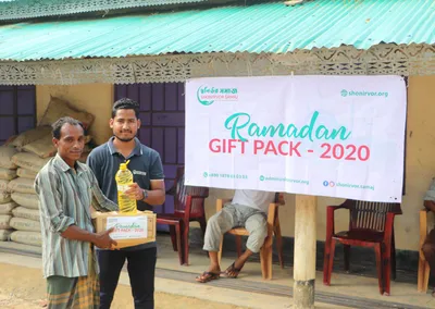 A volunteer handing a Ramadan gift pack and cooking oil to a man