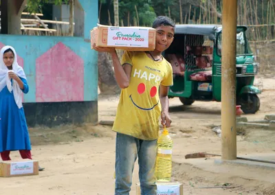 A boy carrying a Ramadan Gift Pack 2020 box and a bottle of cooking oil